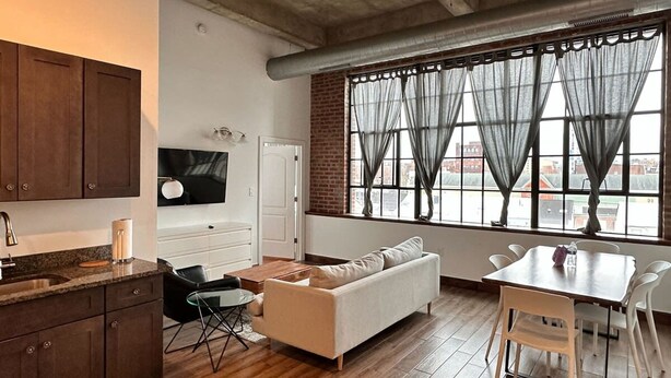 A compact living space with a kitchenette, a sofa, a dining table, and a large window with curtains.