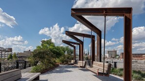 An outdoor seating area with benches and a metal structure, overlooking a cityscape.