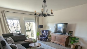 A living room with a sectional sofa, a round coffee table, a TV, and a chandelier.