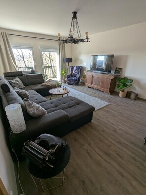 A living room with a sectional sofa, a round coffee table, a TV, and a chandelier. - Apartment 'Am Steinweg' with Mountain View, Private Terrace and Wi-Fi (Solingen)