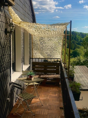 A balcony with a wooden floor, a table with chairs, a potted plant, and a decorative net. - Apartment 'Am Steinweg' with Mountain View, Private Terrace and Wi-Fi (Solingen)