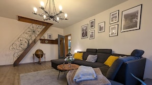 A living room with a staircase, a sofa, a coffee table, and framed pictures on the wall.
