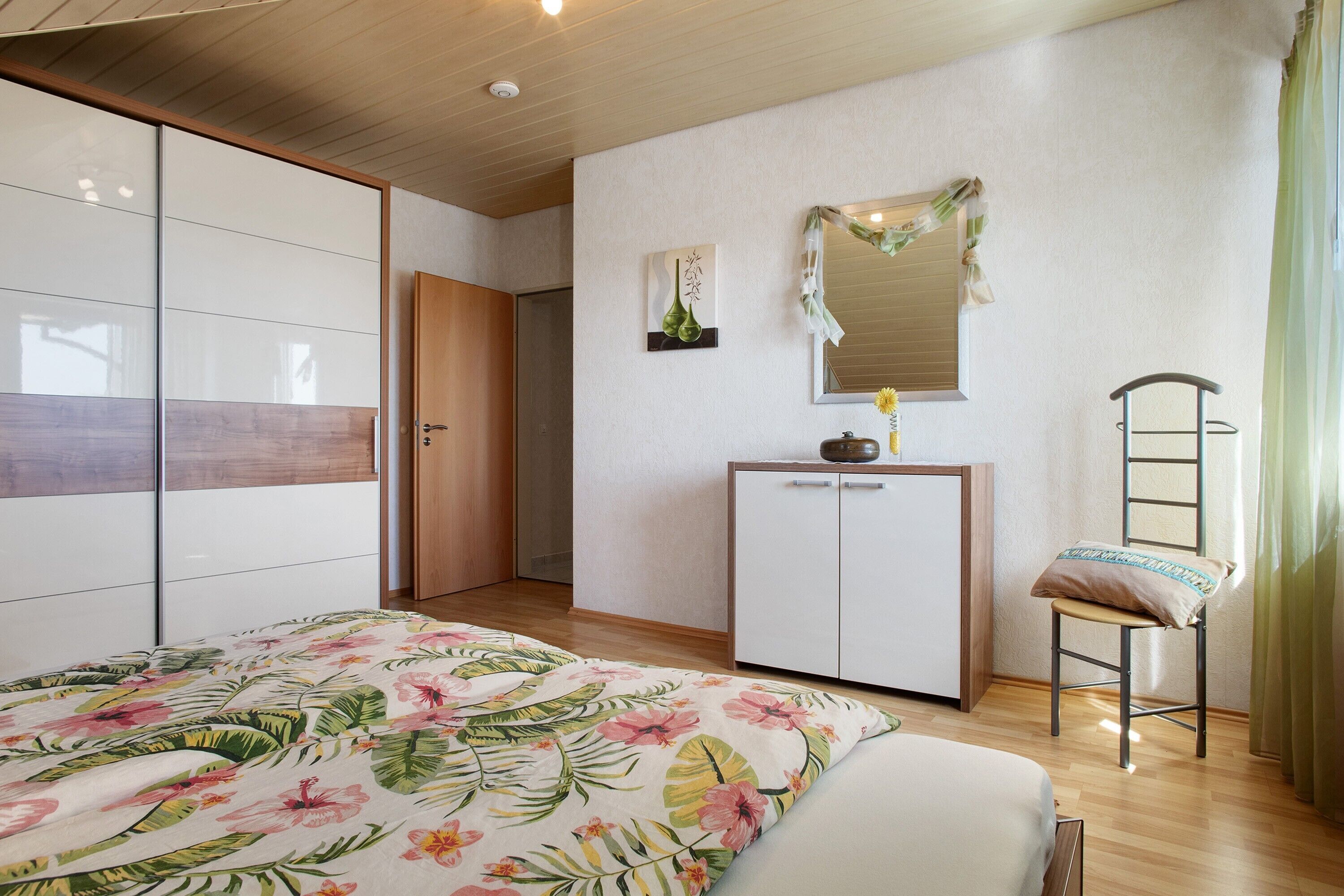 Een slaapkamer met een bed, een kledingkast, een bureau, een stoel en een spiegel.