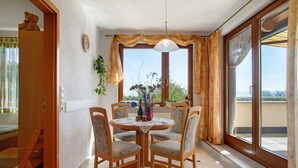 A dining area with a round table, four chairs, a vase with flowers, and a view through large windows. - Apartment 'Plocher' with Lake View, Shared Garden and Wi-Fi (Immenstaad am Bodensee)
