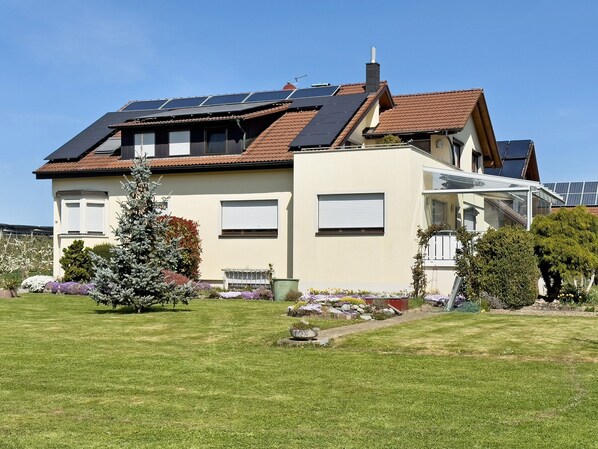 Une maison à deux étages dotée de panneaux solaires, d’une véranda et d’un jardin bien entretenu.