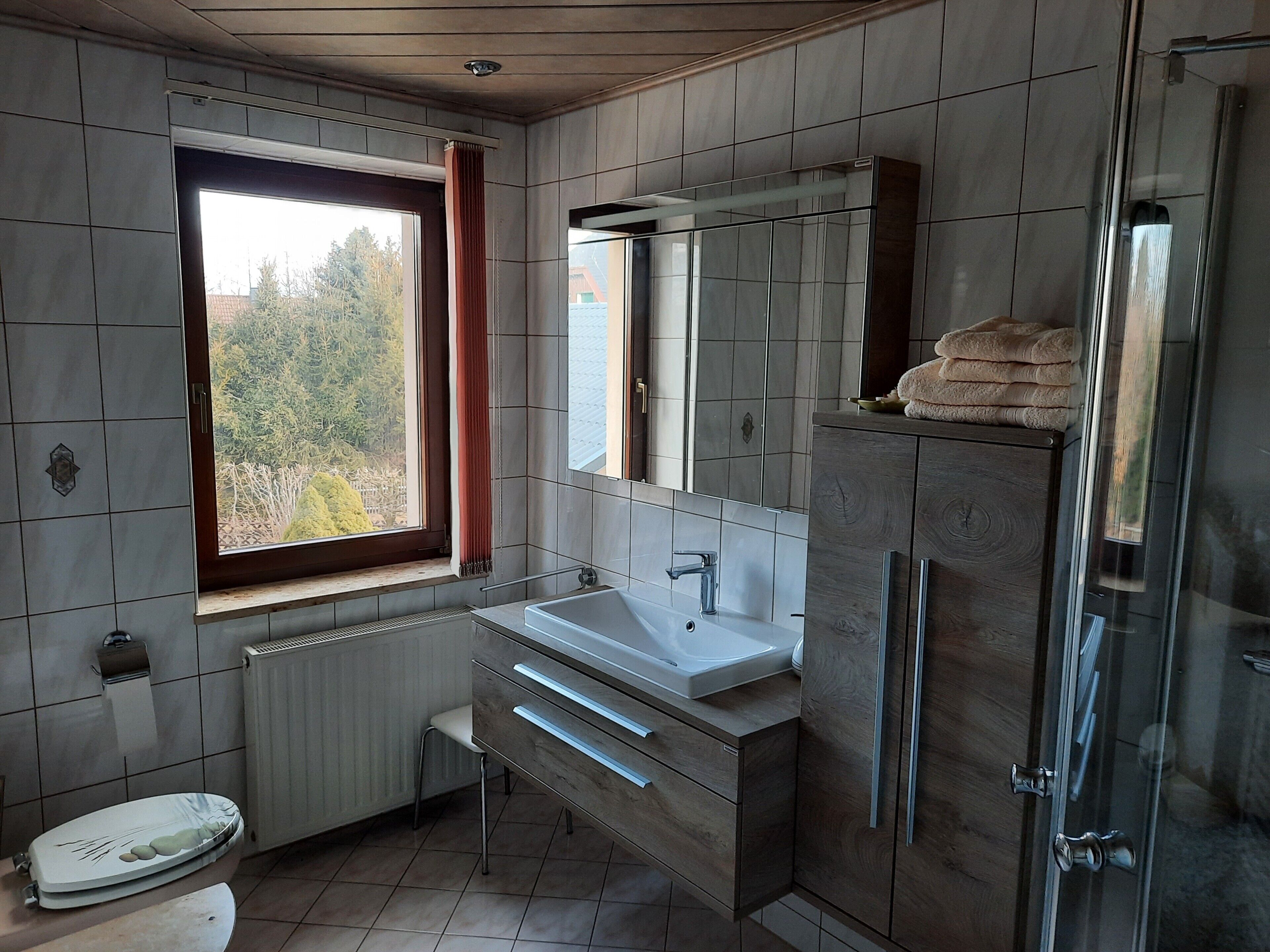 A bathroom with a window, a sink, a mirror, a shower, and a toilet.