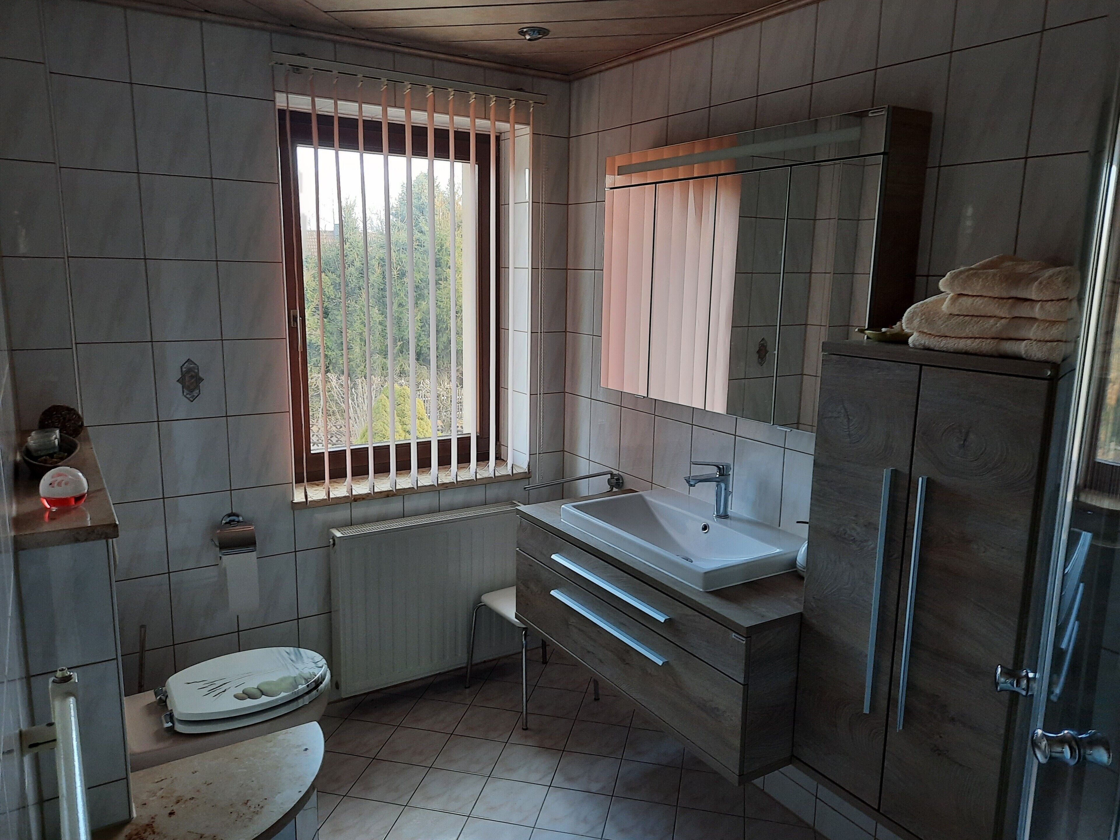 A bathroom with a toilet, sink, mirror, and window with bars.