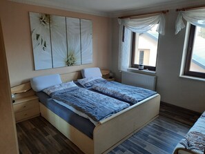 A bedroom with a wooden bed, a nightstand, a wall-mounted lamp, a window with curtains, and a decorative wall piece. - Apartment 'Börner' with Mountain View and Wi-Fi (Frauenstein)