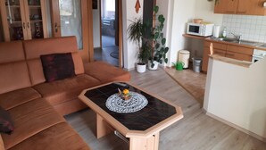 A living room with a sofa, a small coffee table, and a kitchen area with cabinets and a microwave. - Apartment 'Börner' with Mountain View and Wi-Fi (Frauenstein)