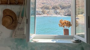 A room with a large window overlooking a coastal landscape, a straw hat, and a whiteboard with writing. - Villa Mariana by Boutique (Folegandros)