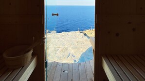 A wooden sauna with a glass door, a wooden bench, and a view of the sea. - Villa Mariana by Boutique (Folegandros)