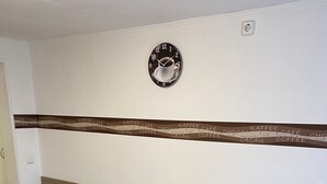 A dining area with a wooden table, two chairs, a wall clock, and a decorative tape with coffee-related words. - Holiday Apartment 'Braun' with Mountain View and Wi-Fi (Lindau)