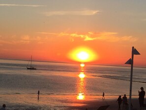 A sunset over a beach with people walking and a sailboat in the distance. - Apartment 'Benekestraße 5 Nr 7' with Balcony and Wi-Fi (Norderney)