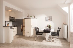 A modern kitchen with a dining area, white cabinetry, a built-in oven, and a dining table with chairs. - Apartment 'Benekestraße 5 Nr 7' with Balcony and Wi-Fi (Norderney)