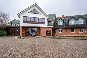 A two-story building with a large entrance, a gravel driveway, and a parking area with marked spaces.