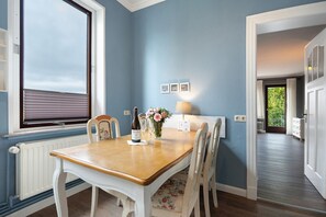 A dining area with a table, chairs, a window with blinds, a lamp, and a vase with flowers.