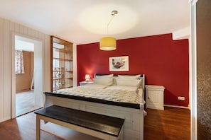 Quarto com cama, mesa de cabeceira, luminária e um banquinho.