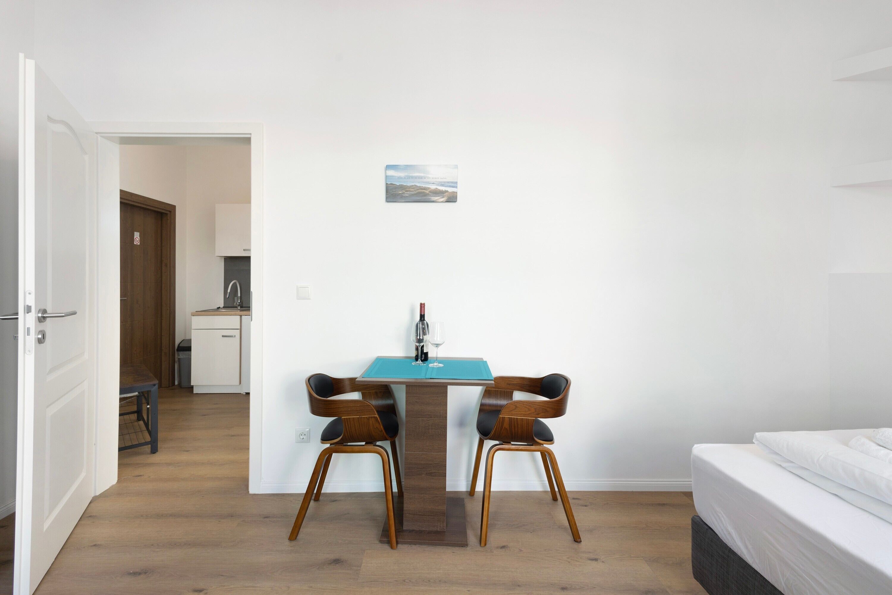 Une pièce comprenant un lit, une table à manger avec des chaises, un petit coin cuisine et une porte donnant sur une autre pièce.