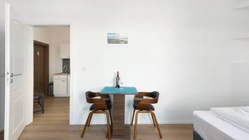 Une pièce comprenant un lit, une table à manger avec des chaises, un petit coin cuisine et une porte donnant sur une autre pièce.