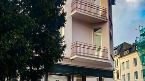 A multi-story building with a staircase leading to an upper floor, a tree in front, and a clear sky.