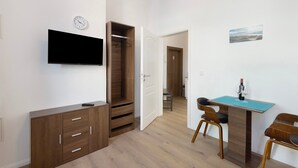 A modern room with a flat-screen TV, wooden wardrobe, and a dining area with a table and chairs.