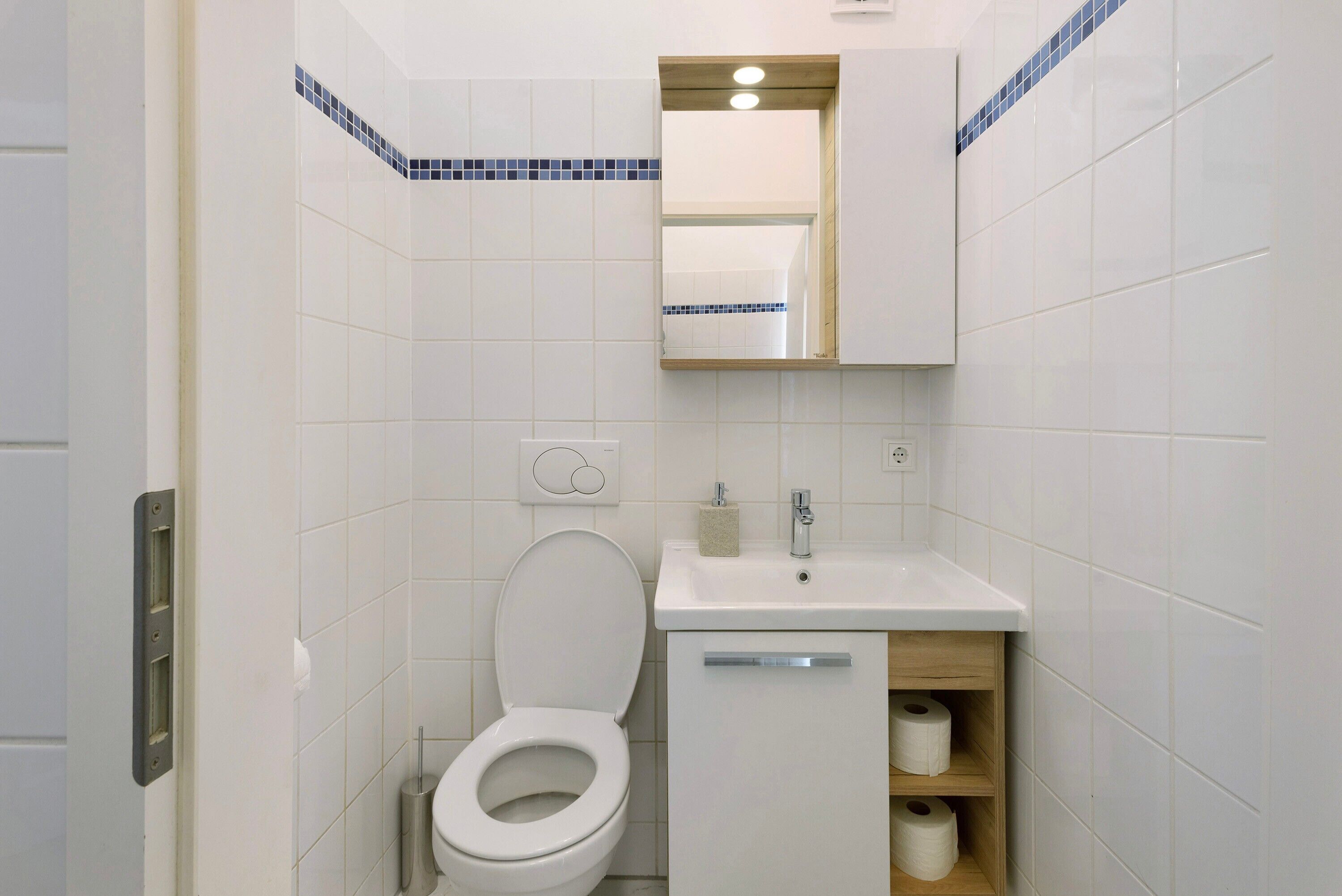 Ein Badezimmer mit Toilette, Waschbecken, Spiegel und Ablagefächern.