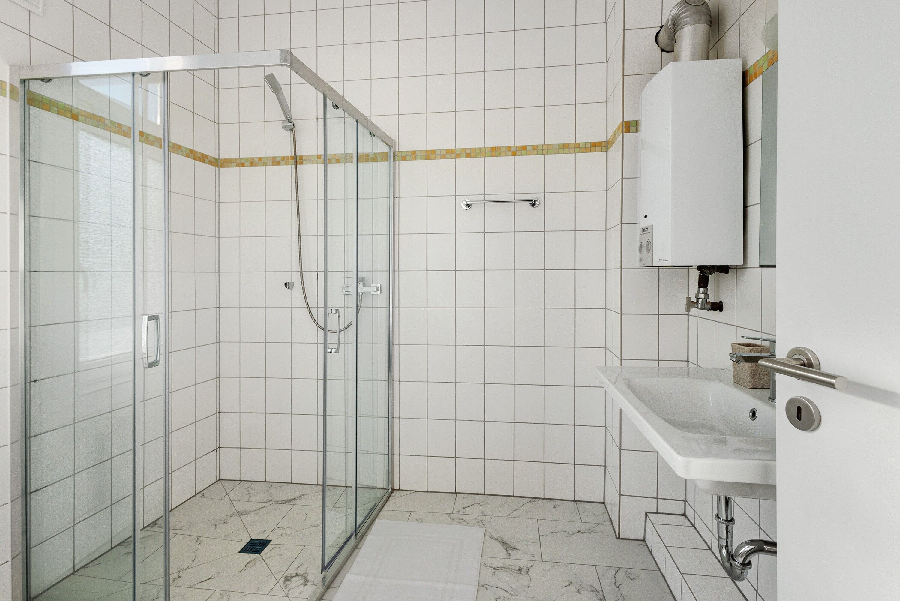 A modern bathroom with a glass shower enclosure, a white sink, and a tiled floor.