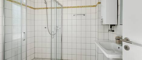 A modern bathroom with a glass shower enclosure, a white sink, and a tiled floor.