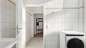 A laundry room with a washing machine, a door leading to another room, and a tiled floor.