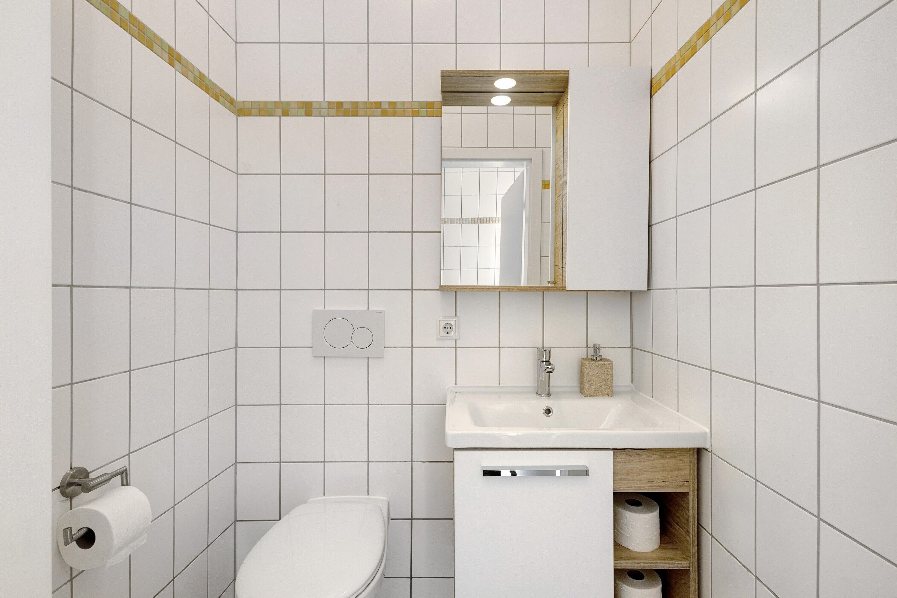 A modern bathroom with white tiles, a toilet, a sink with a mirror, and a towel rack.
