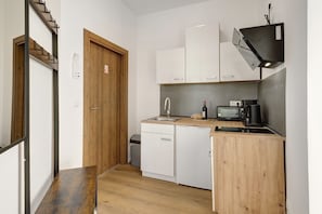 Una cocina compacta con armarios blancos, una puerta de madera, un lavamanos, una cafetera y un tostador.