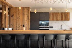 Une cuisine moderne avec un coin bar en bois, des tabourets de bar et des luminaires suspendus.
