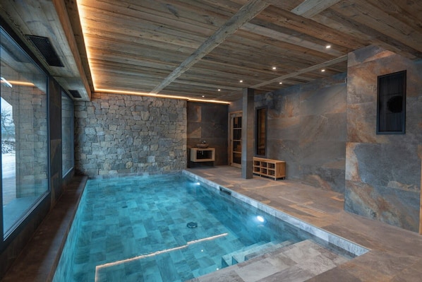 A modern indoor swimming pool with stone walls and wooden beams.