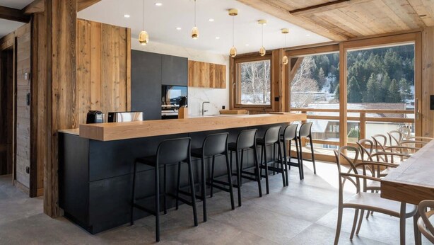 Una cocina moderna con una isla central, taburetes de bar y un área de comedor con vista a un paisaje nevado.