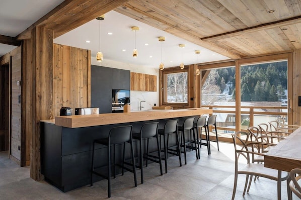 Una cocina moderna con una isla central, taburetes de bar y un área de comedor con vista a un paisaje nevado.