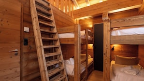 Interior de una cabaña de madera con literas, una escalera y una puerta.