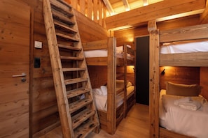 Interior de una cabaña de madera con literas, una escalera y una puerta.