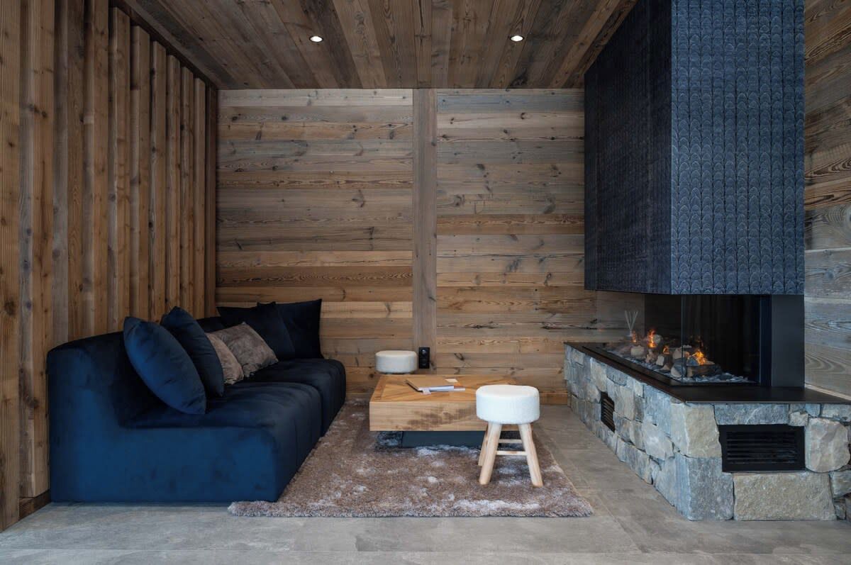 A cozy room with a dark blue sofa, a stone fireplace, and wooden panel walls.