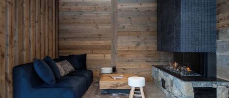 A cozy room with a dark blue sofa, a stone fireplace, and wooden panel walls.