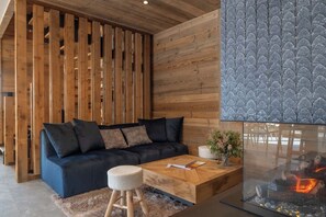 Una sala de estar moderna con un sofá azul oscuro, listones de madera, una mesa de centro de vidrio y una chimenea.