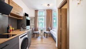 A compact kitchen with a built-in washing machine, a dining area with two chairs, and a view through a window with curtains.