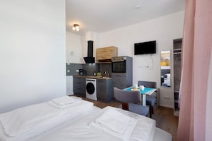 Une chambre d’hôtel compacte comprenant un coin cuisine, un lit, une petite table à manger et un téléviseur.