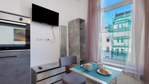 A modern kitchenette with a built-in oven, a flat-screen TV, and a dining area with a table and chairs. - Studio Apartment 3-1 with Wi-Fi (Lübeck)