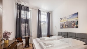 Habitación de hotel con dos camas, un escritorio, una silla, una planta y un cuadro de paisaje urbano en la pared.