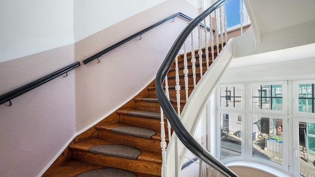 Una escalera de madera con barandilla negra, que lleva a una plataforma con vistas al exterior.