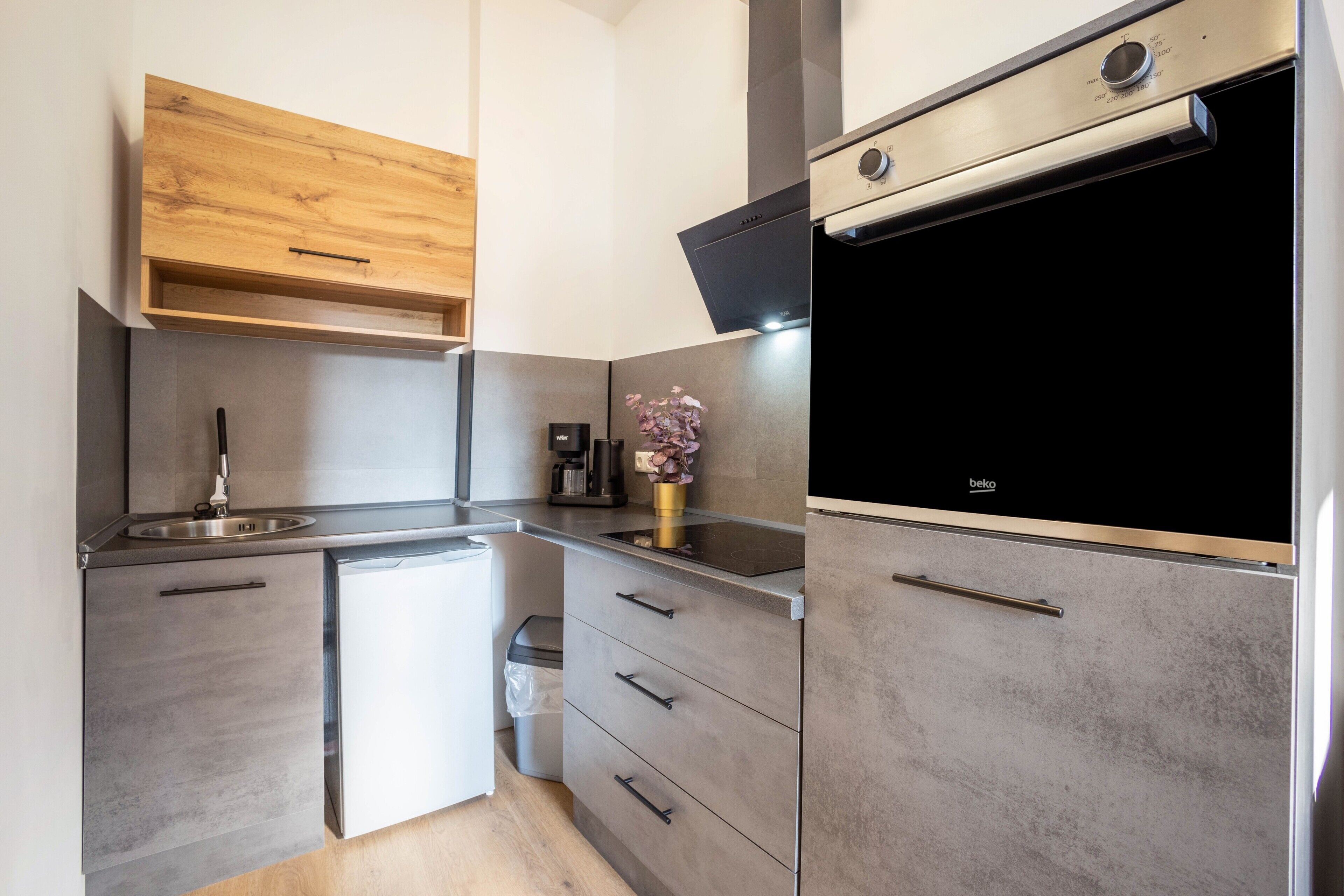 A compact kitchen with a built-in oven, a coffee maker, and a trash bin.