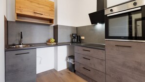 A modern kitchen with grey cabinets, a wooden upper shelf, a built-in oven, and a coffee machine. - 2-bedroom apartment 3-2 with balcony and Wi-Fi (Lübeck)