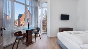 A bedroom with a bed, a desk with chairs, a TV, and large windows with a view of buildings. - 2-bedroom apartment 3-2 with balcony and Wi-Fi (Lübeck)