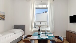 Een slaapkamer met een bed, een eettafel met stoelen, een televisie en een raam met gordijnen.