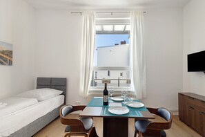 Et soveværelse med seng, et spisebord med stole, et fjernsyn og et vindue med gardiner.